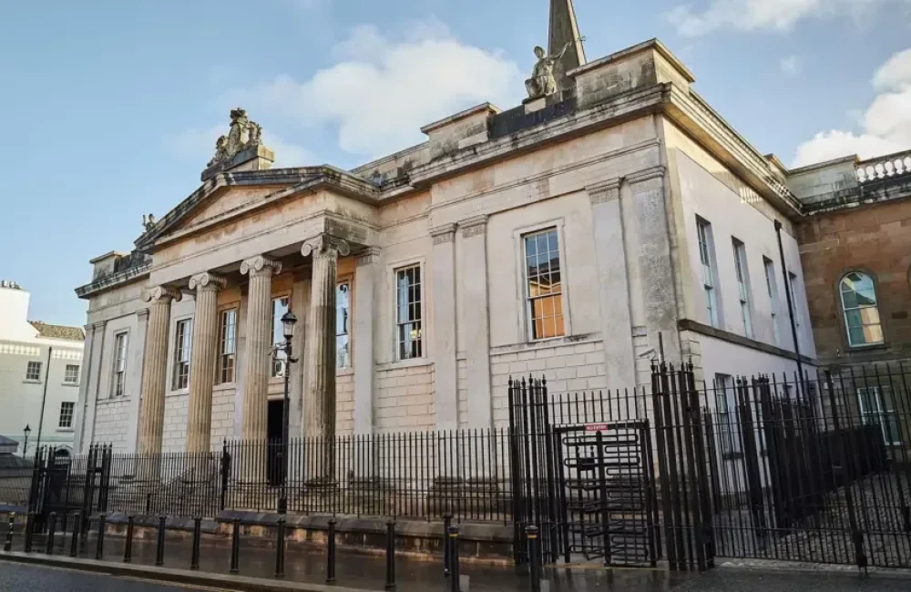 Bishop Street Courthouse is a large marble building with pillars at the front, surrounded by high black gates. A car and a road sign can be seen beside the courthouse.
