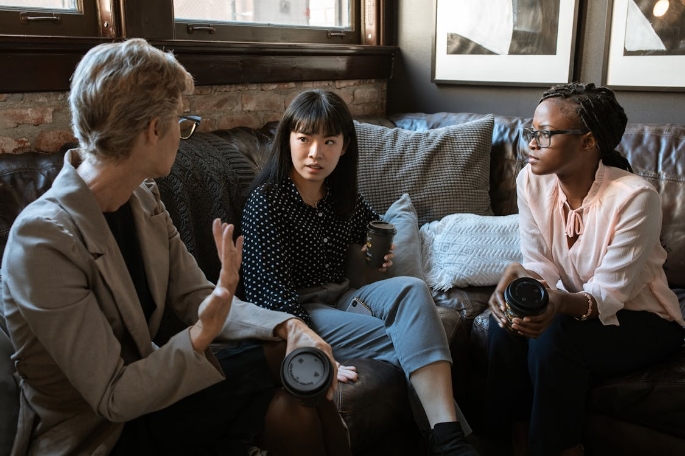 Three women sit together on a sofa in conversation.